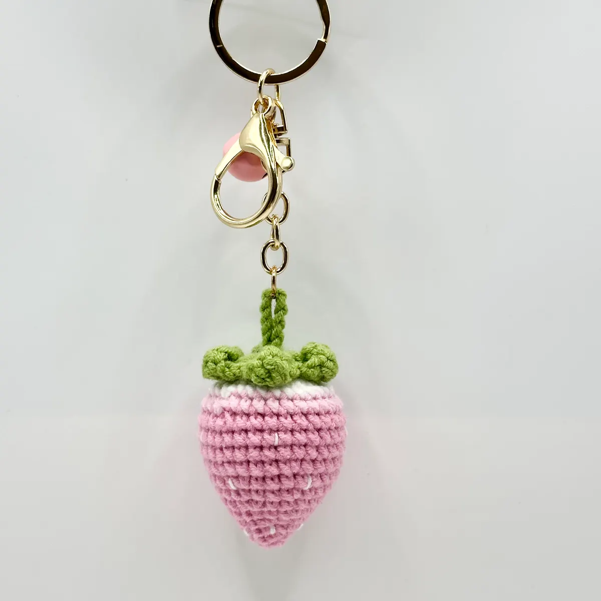 Pink crochet strawberry charm with a green leafy top and a pink bell