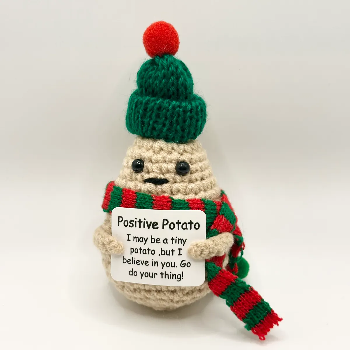 Crochet potato in a green beanie and striped scarf holding a message card