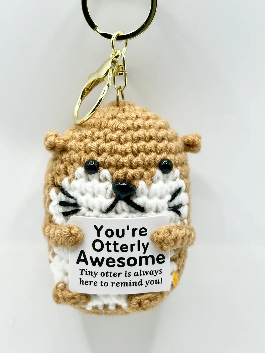 Tan crochet otter keychain holding a You're Otterly Awesome card