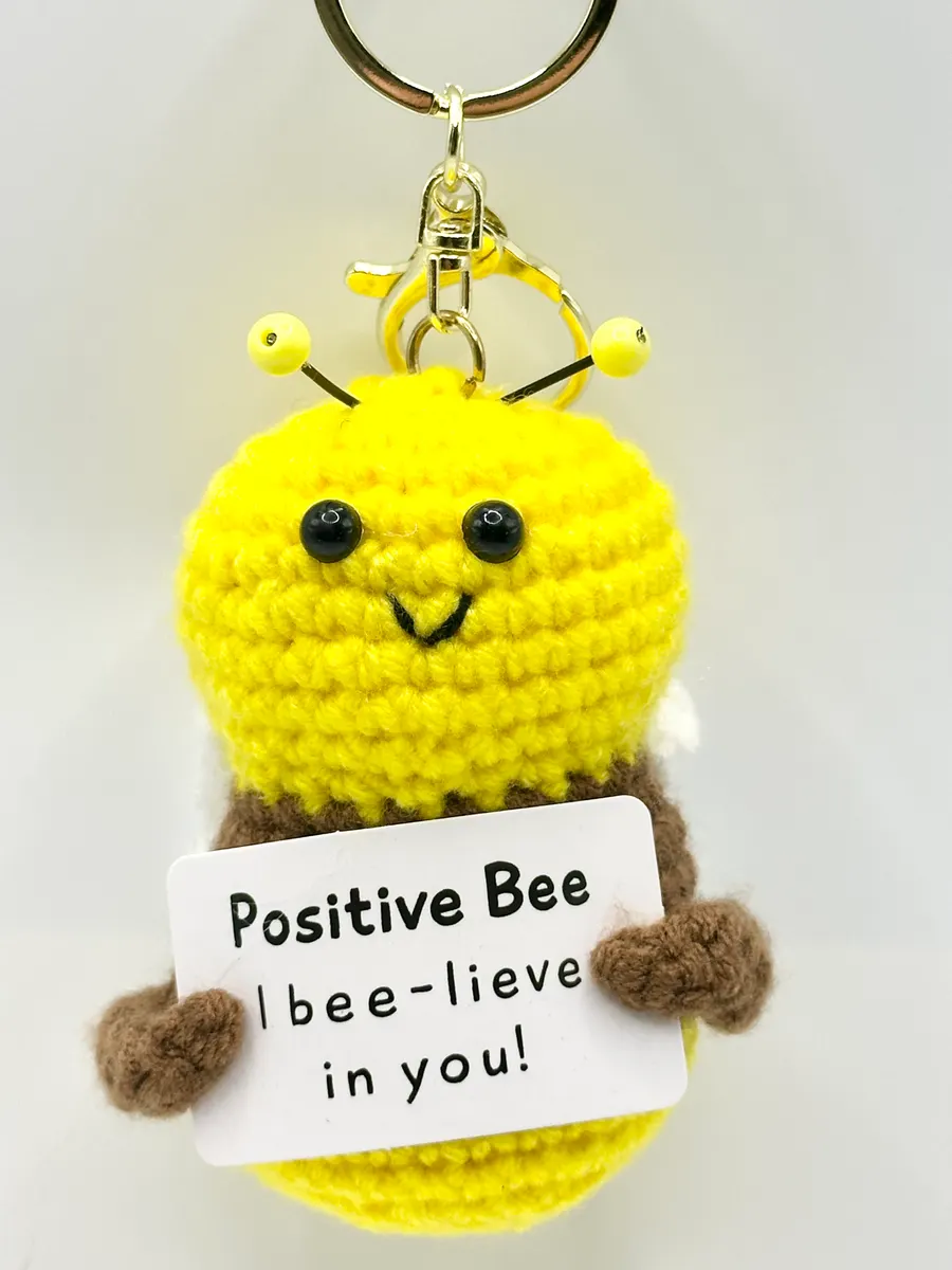 Yellow and brown crochet bee keychain holding a Positive Bee card