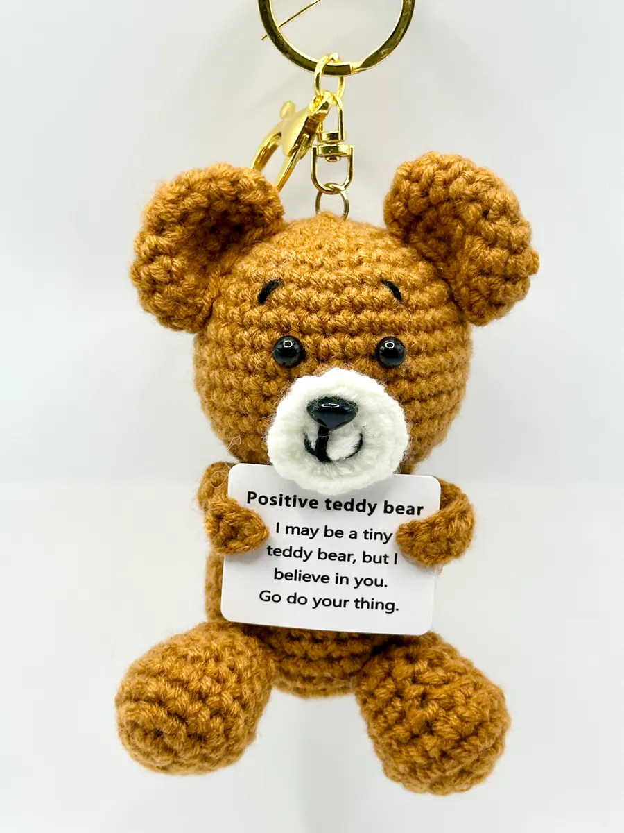 Brown crochet teddy bear keychain holding a positive message card