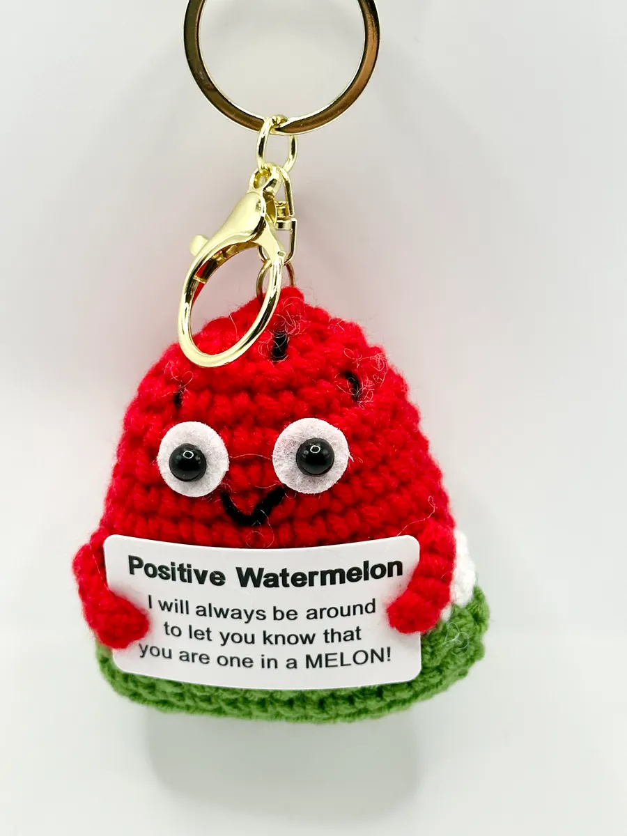 Red and green crochet watermelon keychain holding a Positive Watermelon card