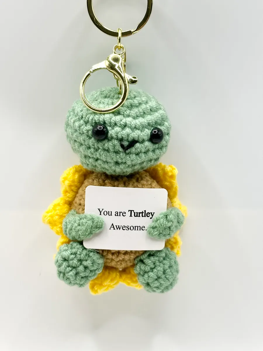 Sage green crochet turtle keychain holding a You are Turtley Awesome card