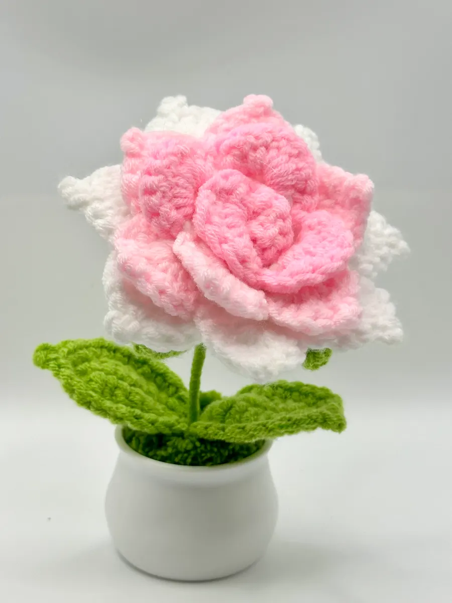 Pink crochet rose with white outer petals on a leafy stem in a small white pot